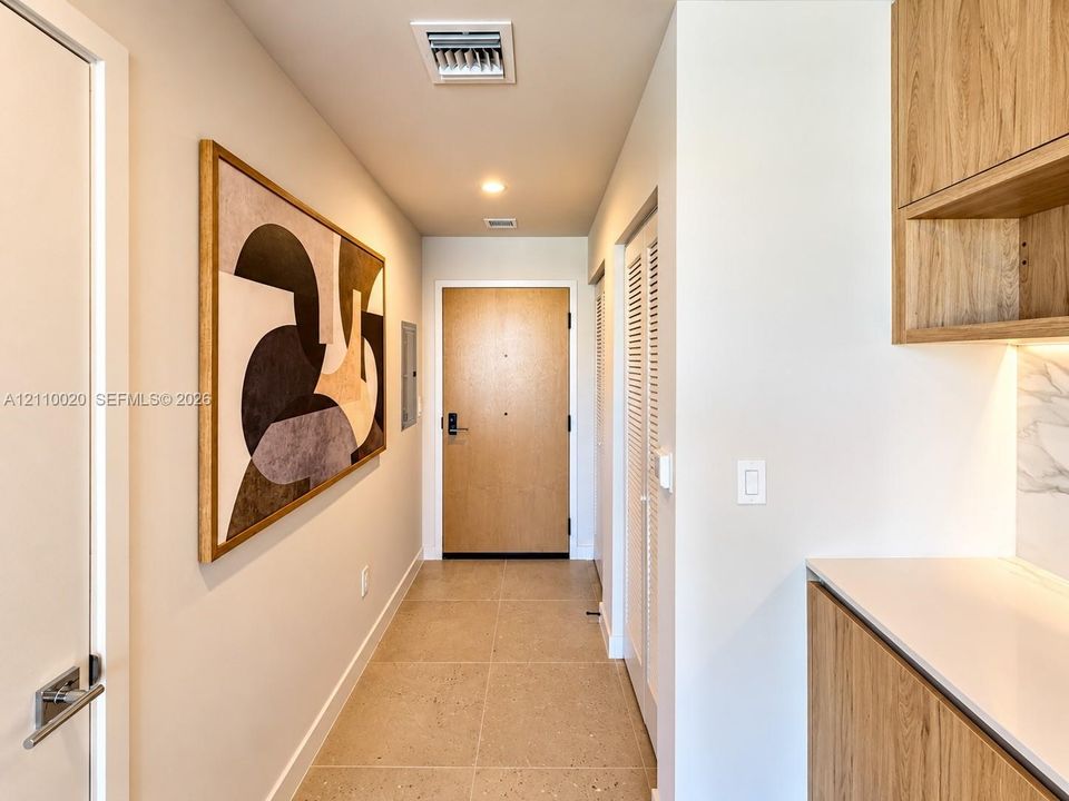 Entryway featuring square-tile flooring, wood-finish cabinetry, white solid-surface countertops, and a wood-veneer entry door