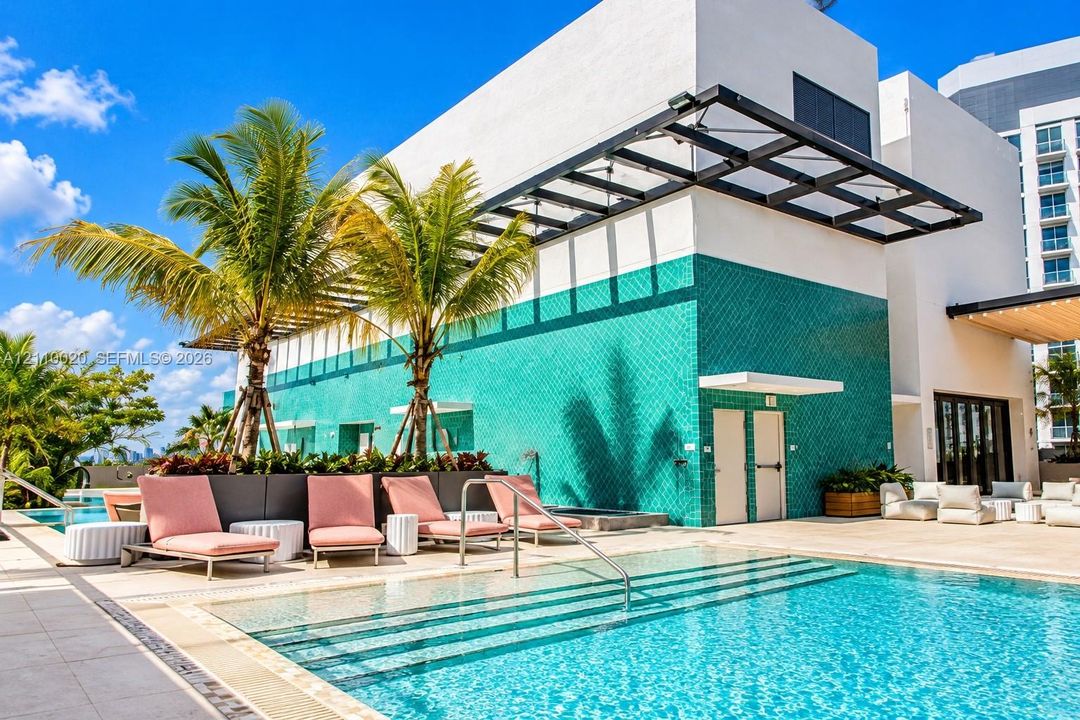 Swimming pool featuring tiered entry steps, teal geometric wall tiling, metal overhead structure, and stone-finish decking