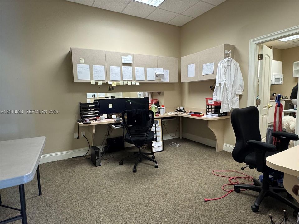 Built-in desk workspace featuring neutral-toned cabinetry, laminate countertops, and acoustic drop ceiling
