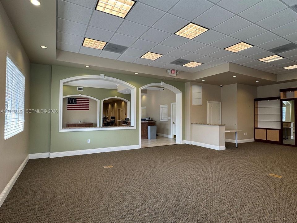 Expansive interior featuring a recessed tray ceiling with integrated drop-tile panels, decorative arched wall cutouts, built-in shelving, and neutral wall-to-wall carpeting