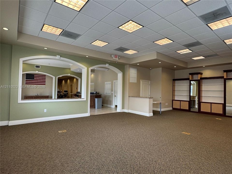 Expansive interior space featuring a drop ceiling with recessed lighting, integrated built-in cabinetry, dual arched wall cutouts, and a neutral color palette