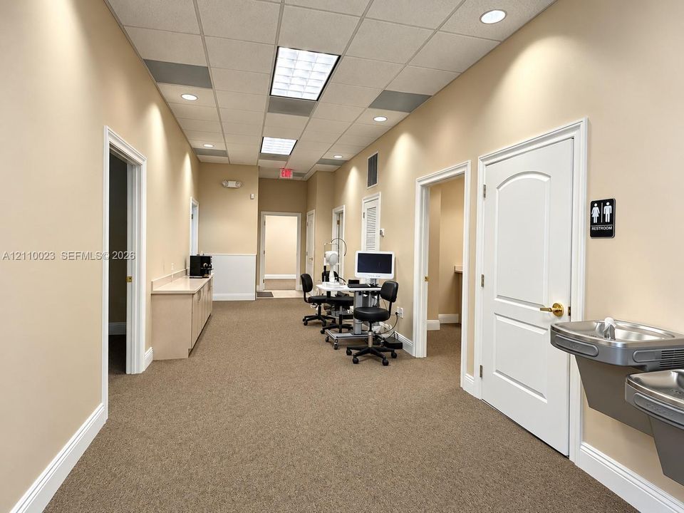 Interior corridor featuring neutral wall finishes, drop ceiling with recessed lighting, carpeted flooring, built-in cabinetry with solid-surface countertop, and a stainless steel water fountain