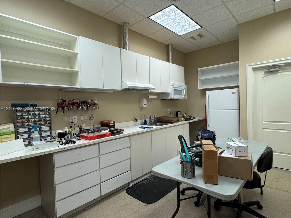 Extensive white cabinetry with upper shelving, solid-surface countertops, built-in sink, and drop-in ceiling lighting