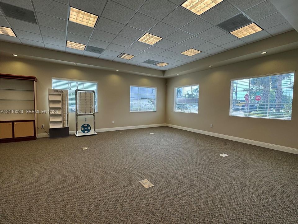 Spacious interior featuring a coffered grid ceiling with recessed panel lighting, neutral wall-to-wall carpeting, multiple windows, and built-in wood cabinetry
