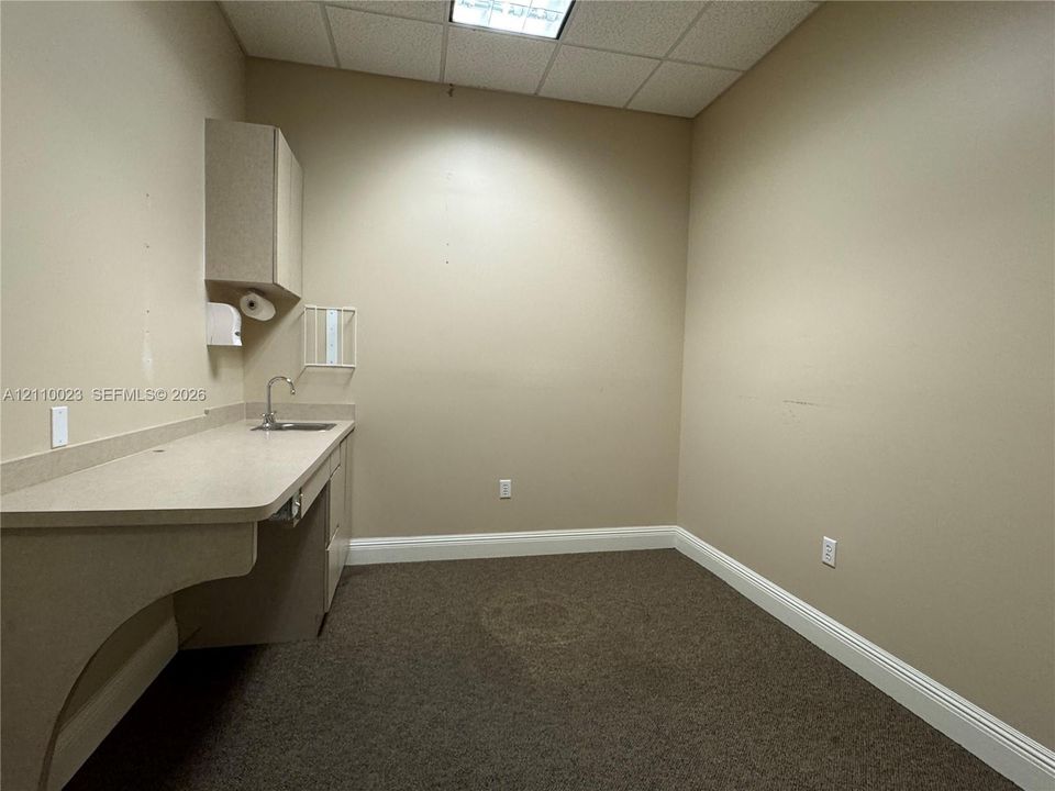 Built-in solid surface countertop with integrated sink, gooseneck faucet, upper wall-mounted cabinetry, and recessed drop ceiling