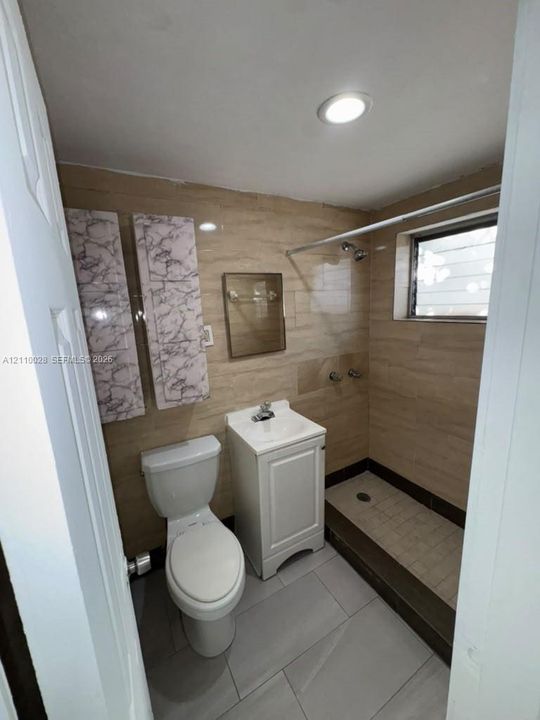 Bathroom featuring floor-to-ceiling stone-finish wall tile, a walk-in shower with a recessed floor, a white pedestal sink, and large-format porcelain tile flooring