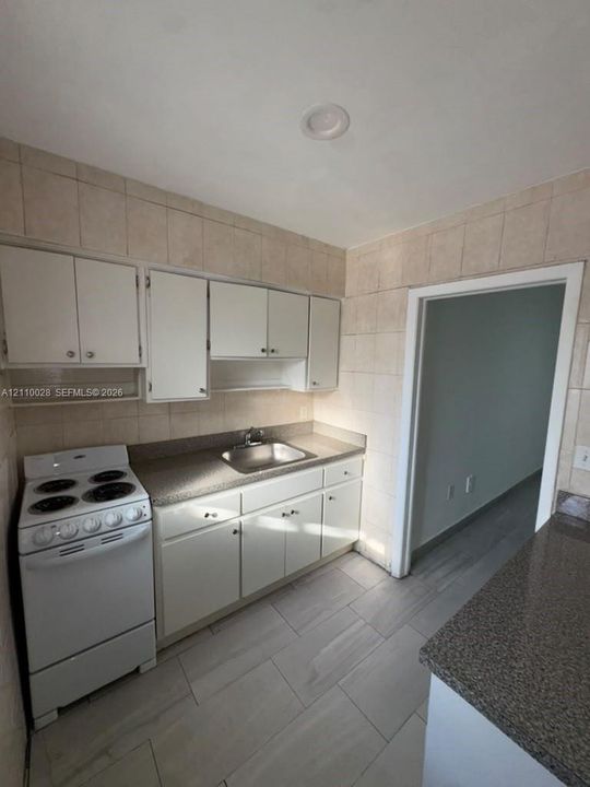 Kitchen featuring white cabinetry, solid surface countertops, stainless steel sink, tile backsplash, and ceramic tile flooring