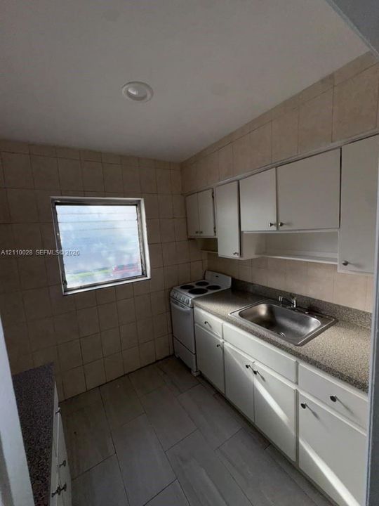 Kitchen featuring white cabinetry, solid-surface countertops, a stainless steel sink, ceramic wall tiling, and tile flooring