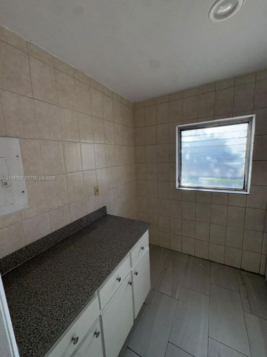 White cabinetry with stone-finish countertops, tile wall cladding, and large-format floor tiling