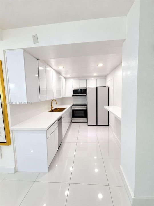 Kitchen featuring high-gloss white cabinetry, quartz countertops, metallic-finish faucet, stainless steel appliances, and large-format tile flooring