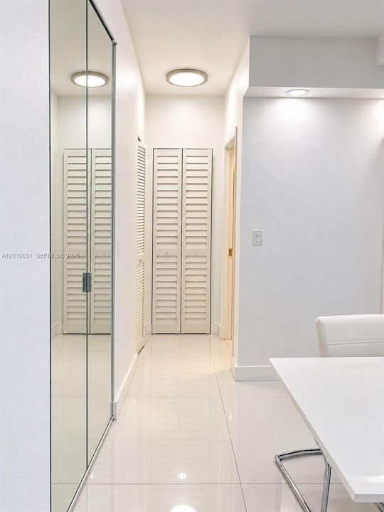 Hallway featuring floor-to-ceiling mirrored sliding closet doors, white louvered bifold closet doors, high-gloss tile flooring, and flush-mount ceiling lighting