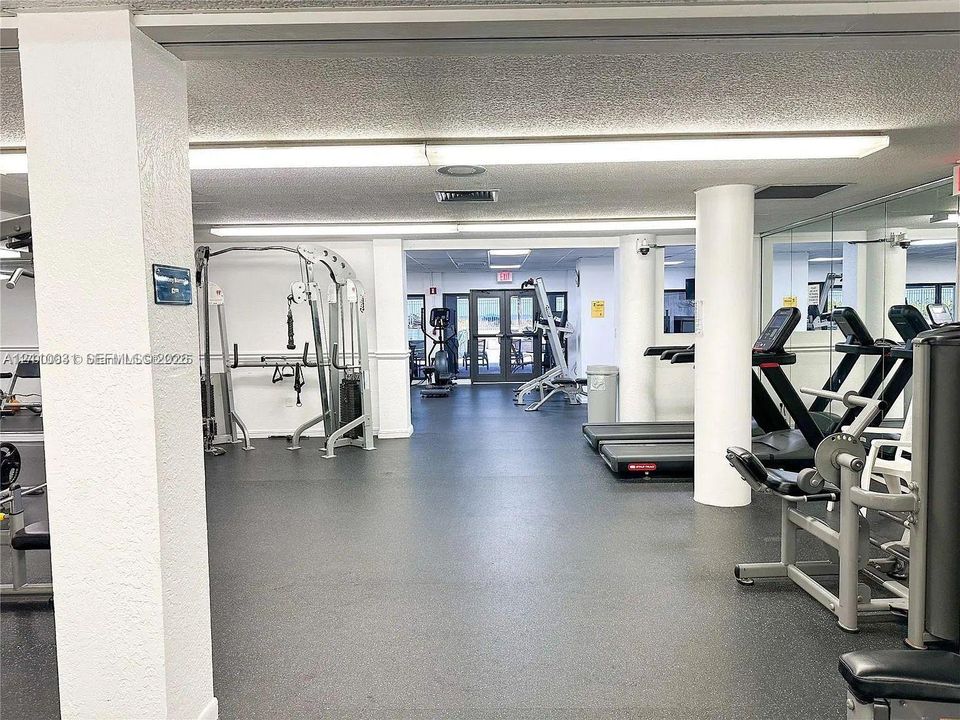 Fitness center featuring rubber flooring, recessed lighting, structural support columns, and mirrored wall panels
