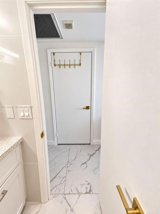 Stone-finish tile flooring, white cabinetry with stone-finish countertop, and brass-tone hardware