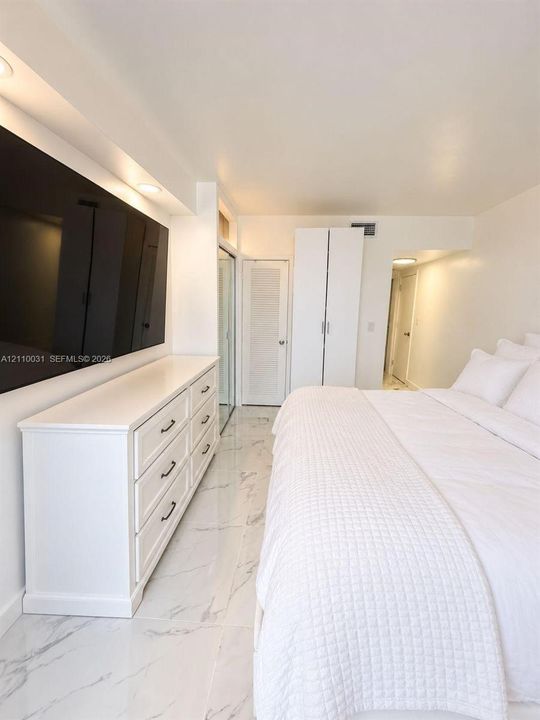 Polished stone-finish flooring, built-in recessed ceiling lighting, louvered closet door, and full-height wardrobe cabinetry