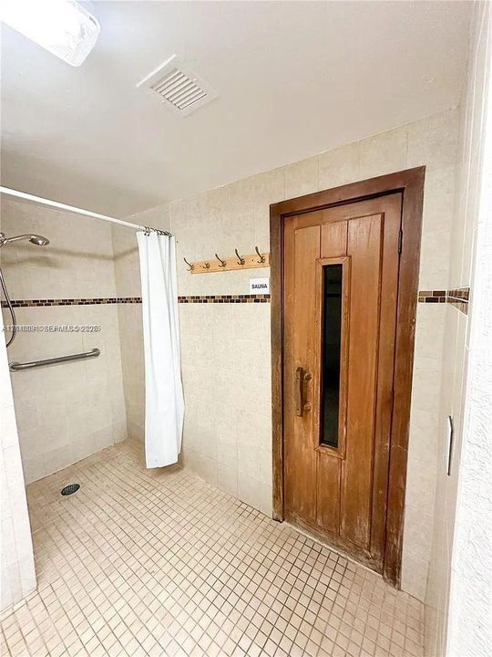 Walk-in shower with a wall-mounted grab bar, tile flooring, and integrated sauna with a wood door