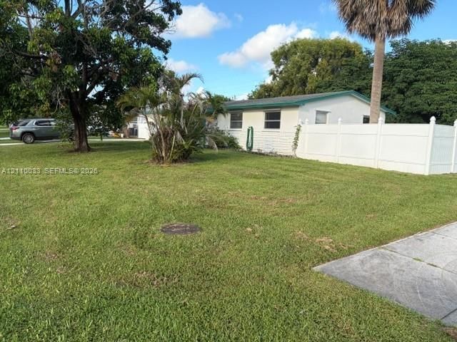 Expansive lawn featuring mature landscaping, palms, and white vinyl perimeter fencing