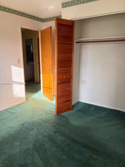 Interior room featuring carpeting, a wood-finish interior door, and a built-in closet with louvered wood-finish doors and a rod-and-shelf configuration