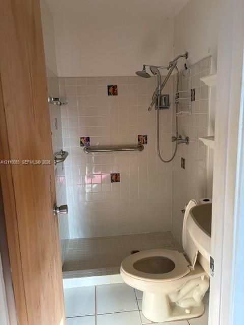Walk-in shower enclosure featuring white ceramic wall tiles with decorative accent inlays, a built-in safety grab bar, a multi-setting shower head, and floor-level tile flooring