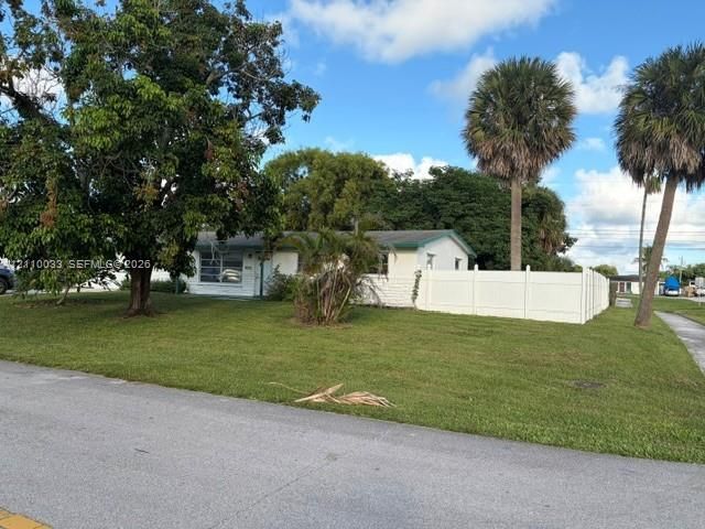 Single-story residence featuring a painted masonry exterior, white vinyl privacy fencing, and mature landscaping