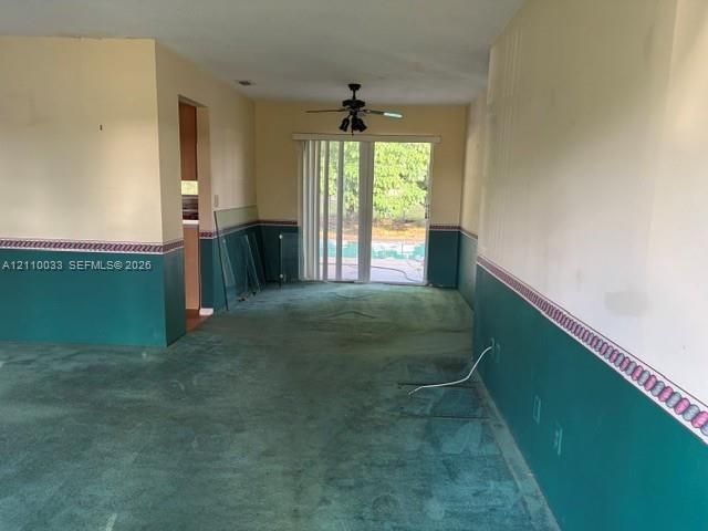 Carpeted flooring, dual-tone wall treatment with decorative border, ceiling-mounted fan with light fixture, and sliding glass doors