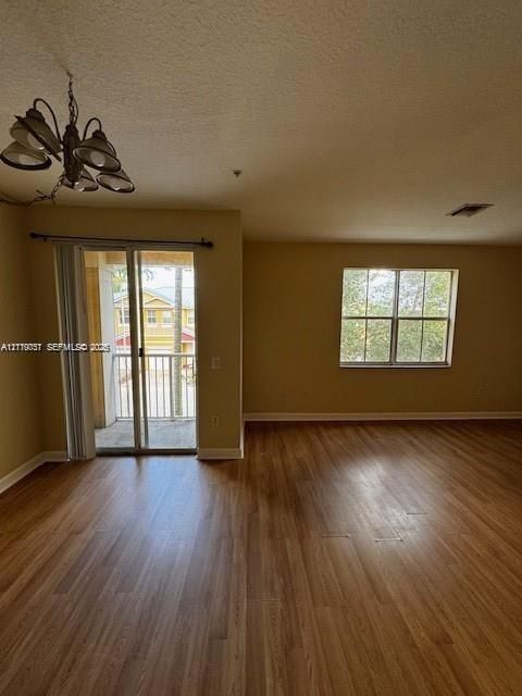 Wood-finish flooring, sliding glass door to a private balcony, multi-pane window, and a multi-light metal chandelier