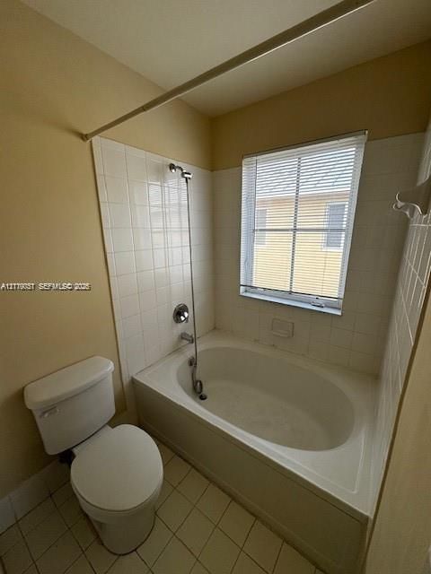 Built-in soaking tub with white tile surround, chrome hand-held shower fixture, and a window providing natural light