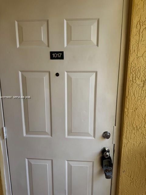Four-panel entry door featuring a matte black door number plaque, a centered peephole, and a metallic knob and deadbolt hardware set