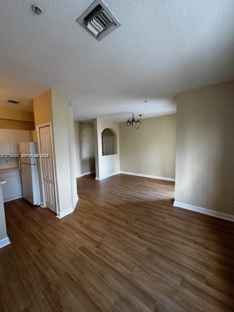 Interior featuring wood-finish flooring, white cabinetry, arched architectural alcove, and multi-light hanging chandelier