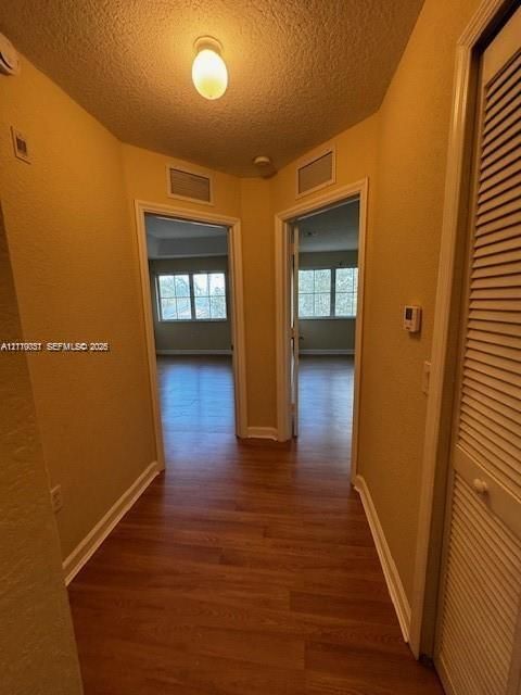 Hallway featuring wood-finish flooring, textured ceilings, flush-mount lighting, and a built-in louvered closet door