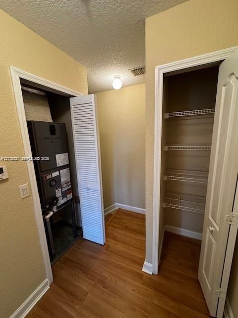 Utility space featuring wood-finish flooring, a louvered-door mechanical closet, and a secondary closet with built-in wire shelving