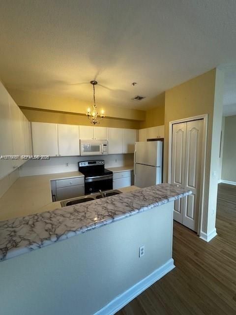 Kitchen featuring white cabinetry, stone-finish breakfast bar, wood-finish flooring, and a multi-bulb hanging light fixture