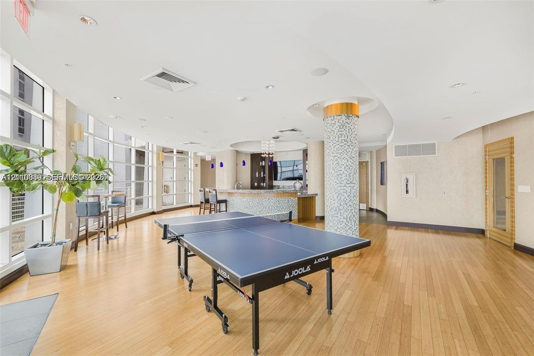 Recreational area featuring wood-finish flooring, floor-to-ceiling windows, a mosaic-tiled structural column, and a built-in wet bar with cabinetry