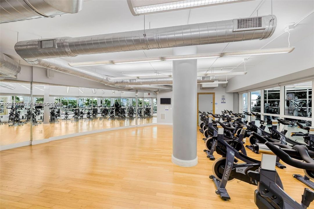 Industrial aesthetic featuring exposed metal ductwork, full-wall mirrors, light wood-finish flooring, and linear LED lighting