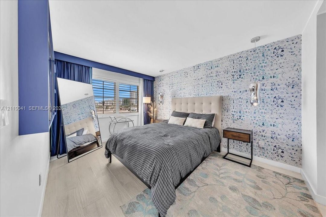 Bedroom featuring wood-finish flooring, decorative patterned wall covering, recessed ceiling lighting, and suspended metallic pendant light fixtures