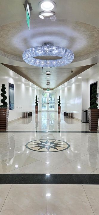 Grand entryway featuring a polished stone floor with an inlaid star medallion, a large circular crystal chandelier, recessed ceiling lighting, and symmetrical tray ceiling detailing
