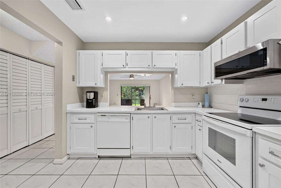 Kitchen featuring white shaker-style cabinetry, solid-surface countertops, recessed lighting, tile flooring, and a passthrough window