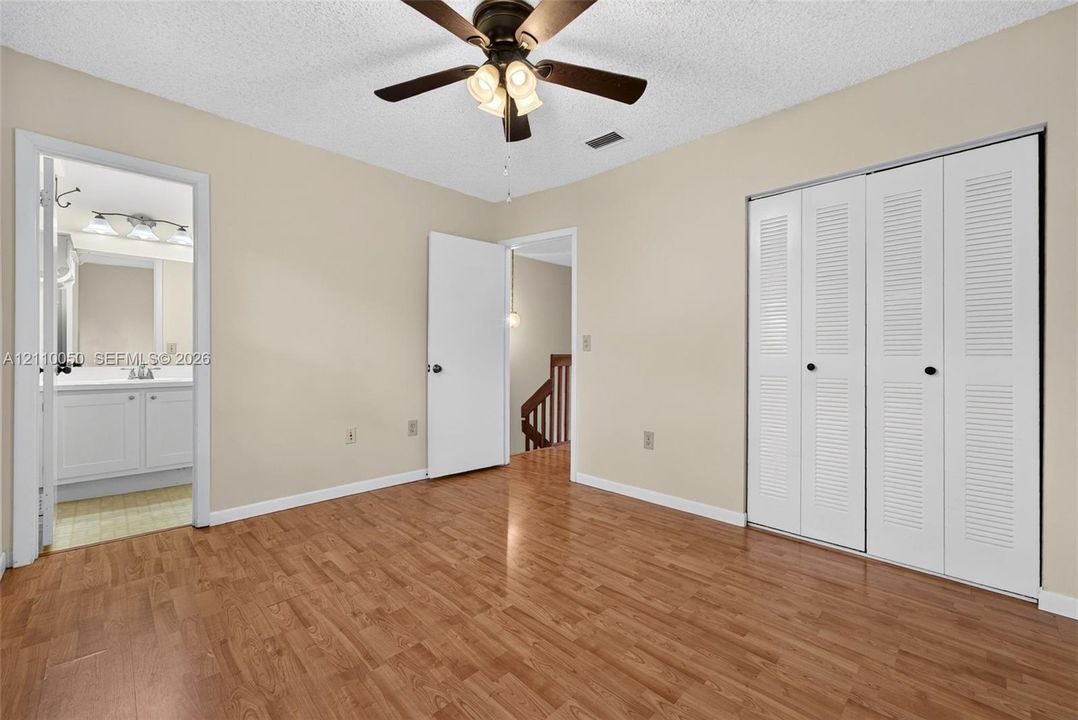 Room featuring wood-finish flooring, a ceiling fan with integrated lighting, and a closet with white louvered bifold doors