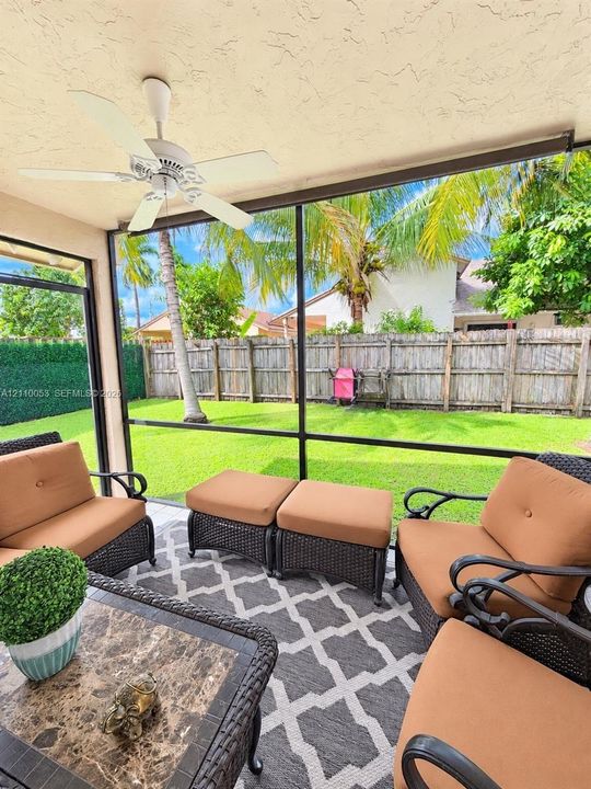 Screened lanai featuring a ceiling-mounted fan and tile flooring, providing an enclosure for the expansive backyard with a manicured lawn and wood-panel fencing