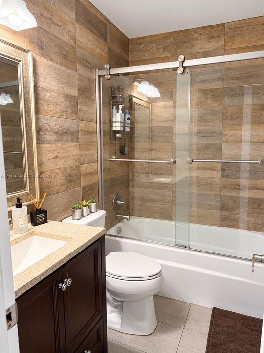 Dark wood vanity with a solid surface countertop and undermount sink, wood-finish tile wall accents, and a sliding glass shower door enclosure