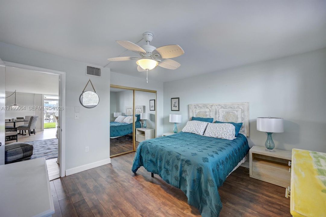 Bedroom featuring wood-finish flooring, a multi-blade ceiling fan with integrated lighting, and dual floor-to-ceiling mirrored closet doors
