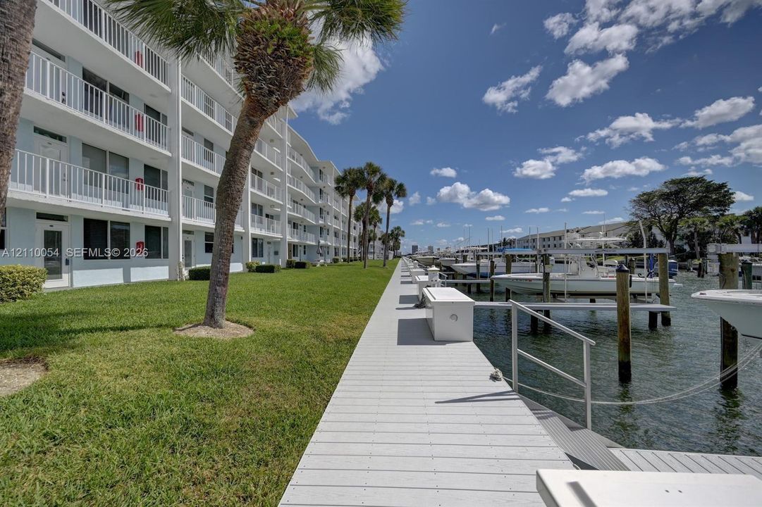 Waterfront property featuring a private boat dock, manicured green space, palm trees, and multi-level exterior balconies