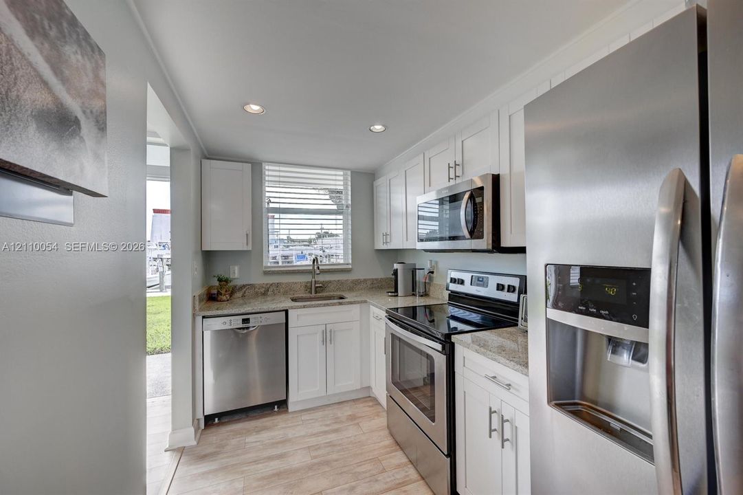 Kitchen featuring white shaker-style cabinetry, stone-surface countertops, stainless steel appliances, and wood-finish flooring