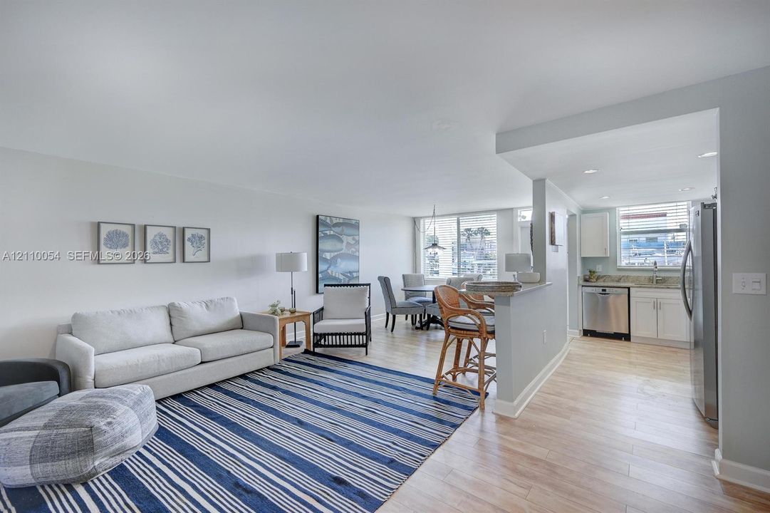 Open-concept interior featuring wood-finish flooring, a kitchen breakfast bar, recessed lighting, and white cabinetry