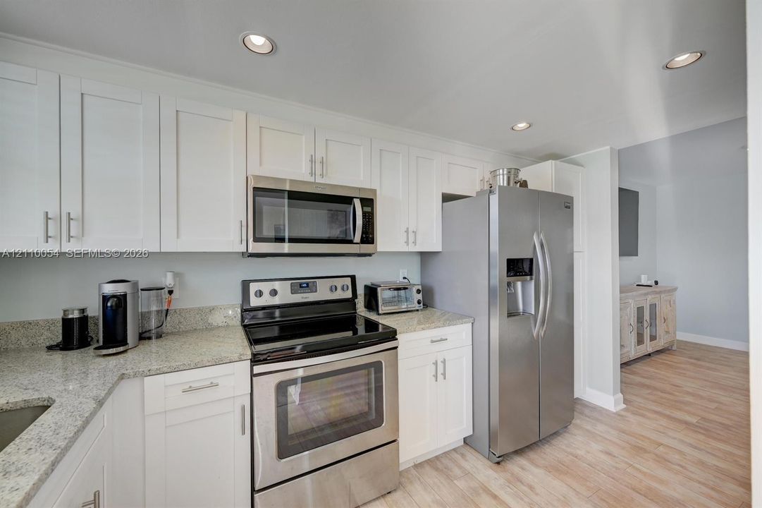 Kitchen featuring white shaker-style cabinetry, stone-finish countertops, stainless steel appliances, recessed ceiling lighting, and wood-finish flooring