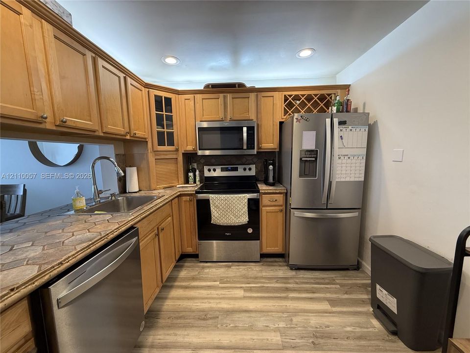 Kitchen featuring wood cabinetry, stainless steel appliances, integrated wine rack, tile countertops, and recessed lighting