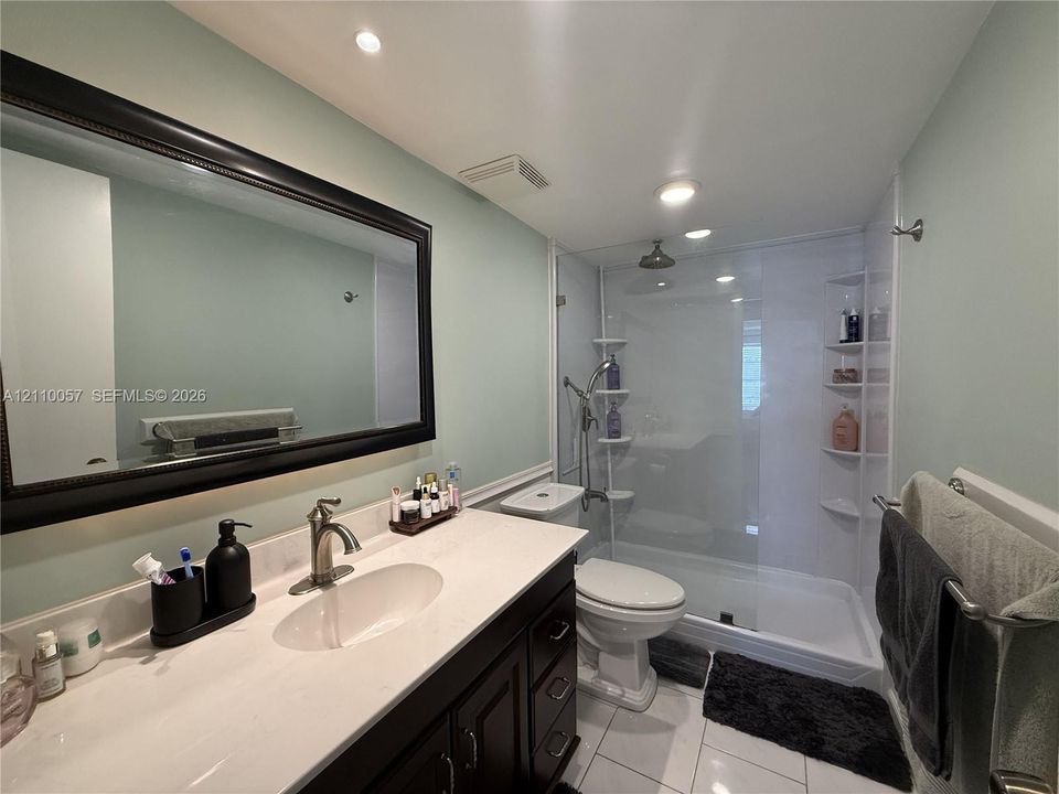Bathroom featuring a dark wood vanity with a light-toned countertop, an integrated oval sink, a large framed mirror, and a walk-in shower with a glass enclosure