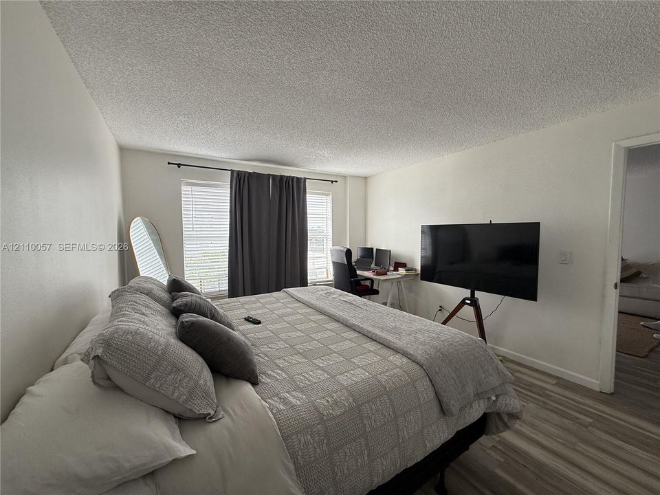 Room featuring textured ceiling, dual windows with black curtain hardware, and wood-finish flooring