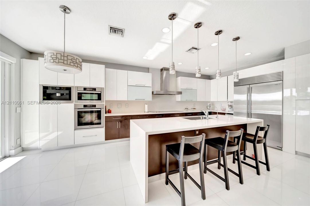 Contemporary kitchen featuring high-gloss cabinetry, a central island with a solid surface countertop, stainless steel appliances, and pendant lighting