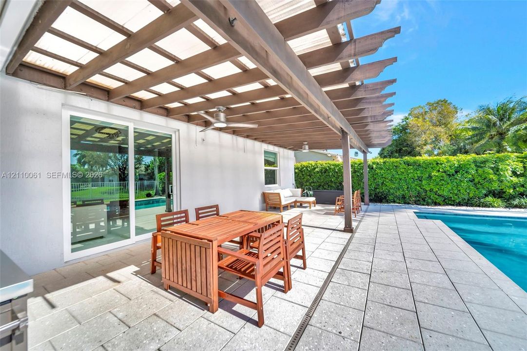 Covered patio featuring a timber pergola, built-in ceiling fans, stone paver flooring, and a swimming pool with a perimeter hedge
