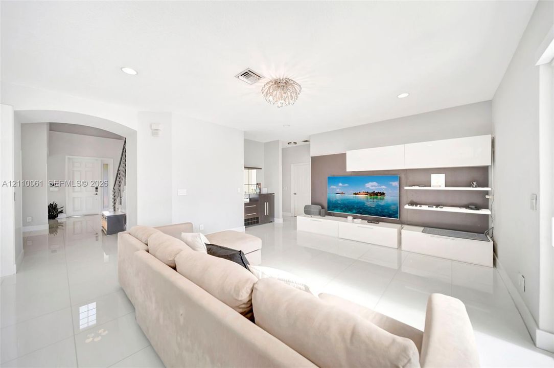 Large-format polished tile flooring, integrated wall-mounted media cabinetry with open shelving, recessed lighting, arched entryway, and decorative flush-mount ceiling fixture